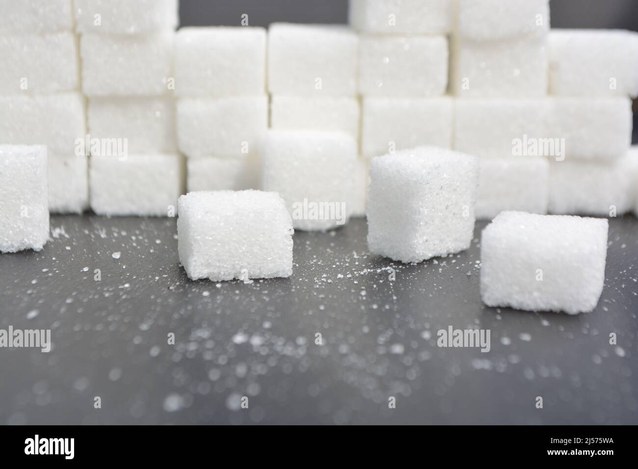 Passi fatti da cubetti di zucchero. Mucchio di cubetti di zucchero su una superficie grigia lucida, piramide di zucchero. Foto Stock