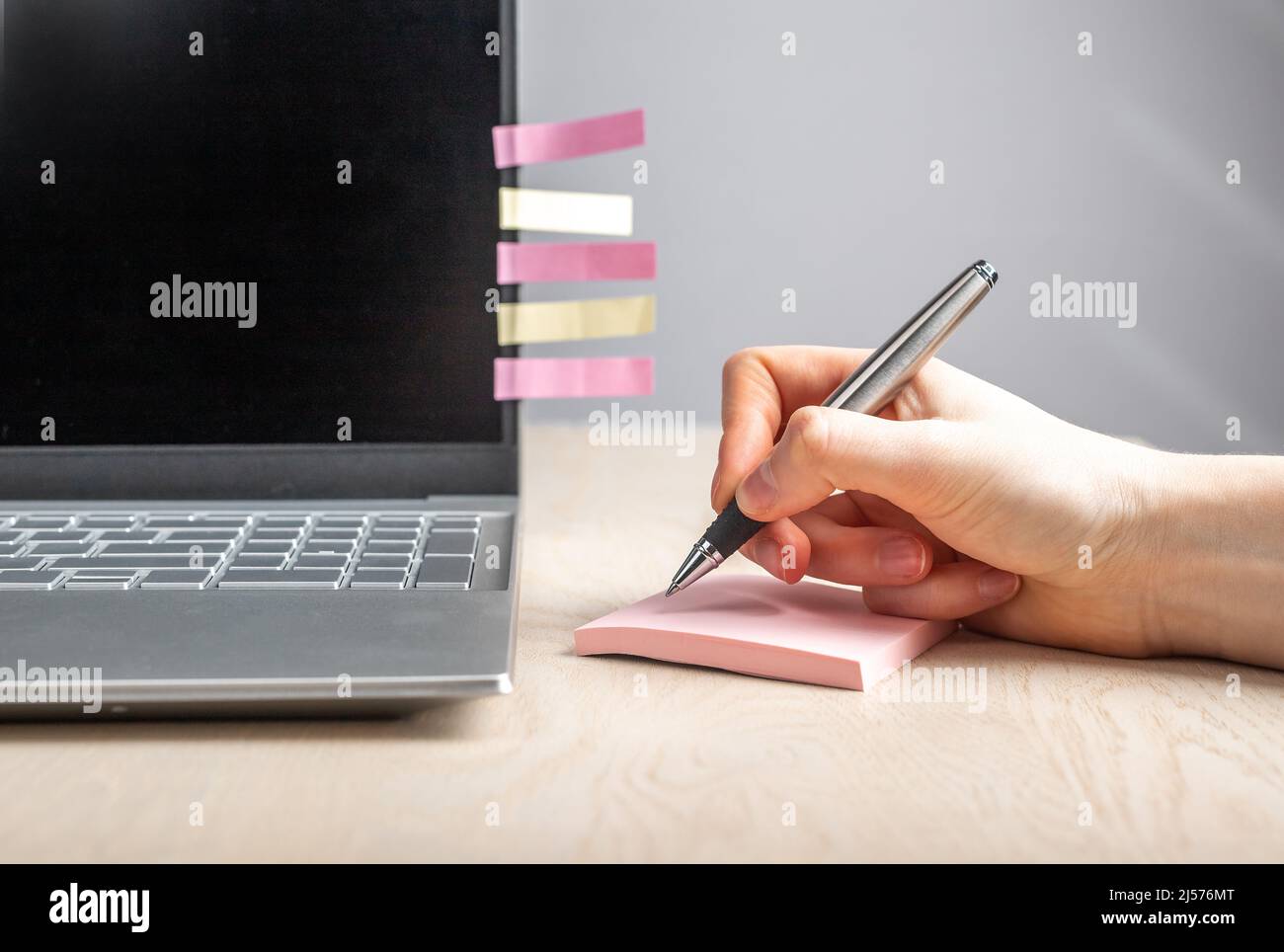 Donna mano scrivere promemoria a note appiccicose. Donna seduta alla scrivania con computer portatile e registrazione con parole chiave penna e frasi. Foto di alta qualità Foto Stock