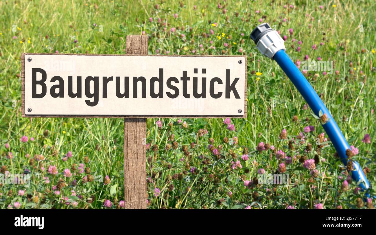 Segno con la parola tedesca 'Baugrundstück' (edificio trama) e acqua potabile per la vostra casa su un prato verde. Foto Stock