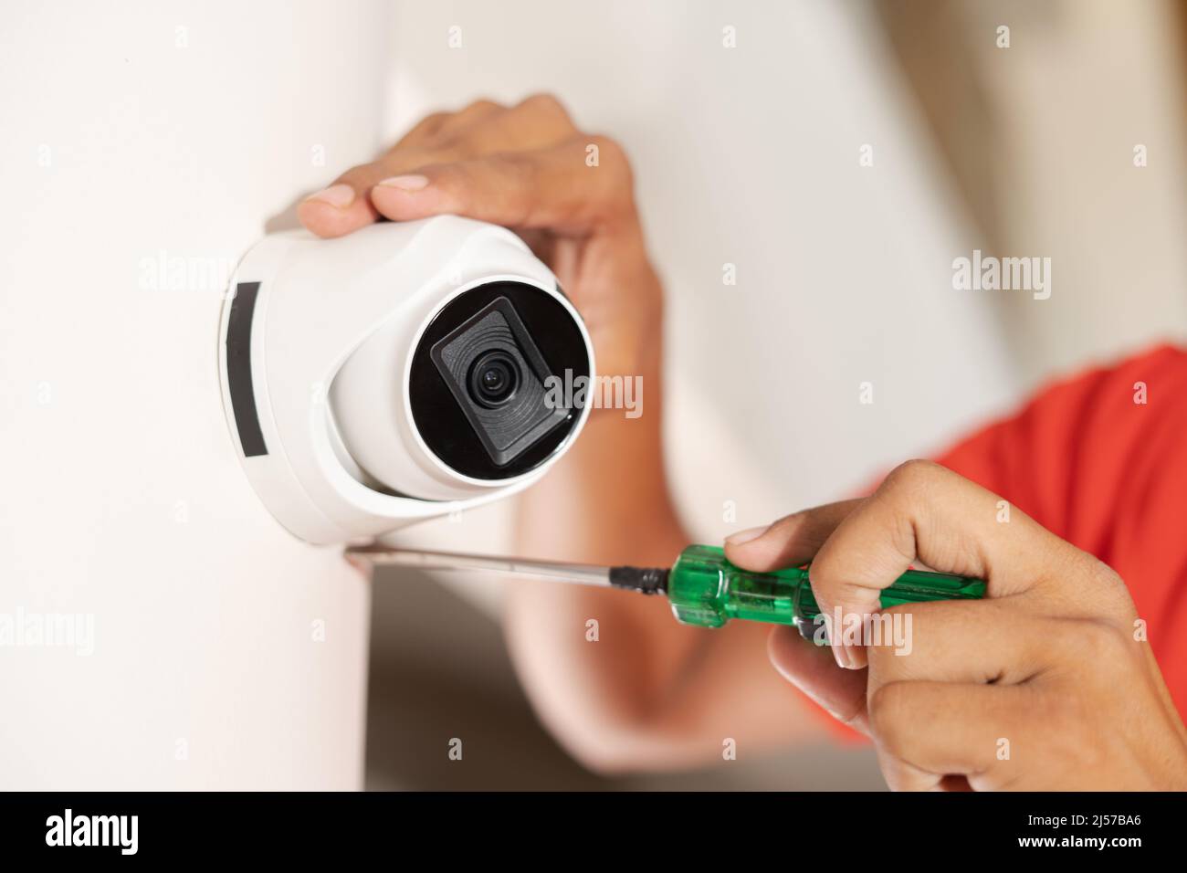 Primo piano del tecnico che fissa la telecamera tvcc a parete a casa - concetto di sicurezza, lavoratore professionale e servizio di manutenzione Foto Stock