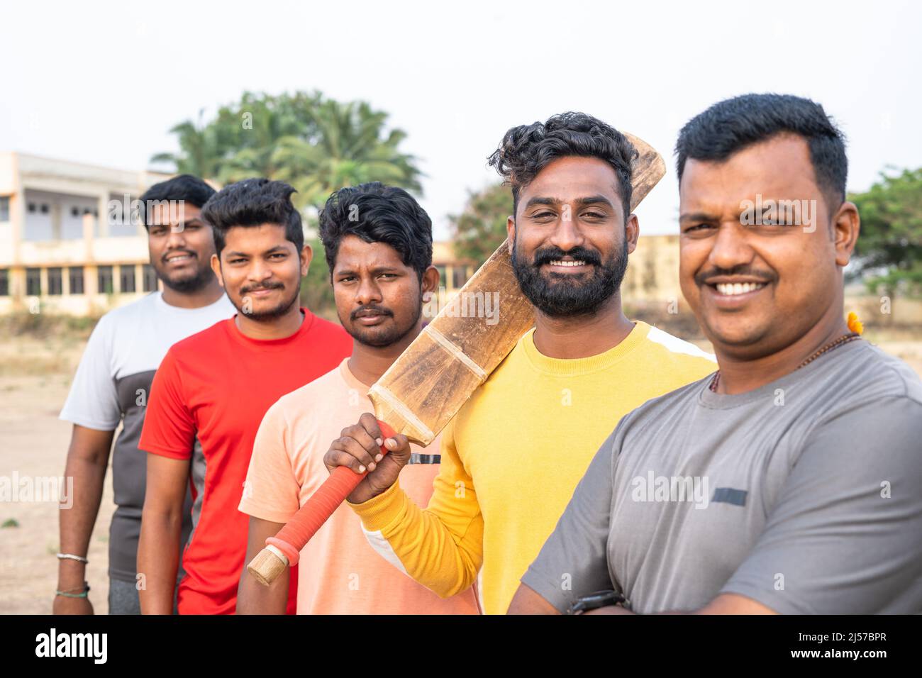 Concentratevi su battitore, che guarda la macchina fotografica tenendo la mazza mentre siete in piedi con la squadra di cricket - gruppo di giocatori locali, atletica e competizione Foto Stock