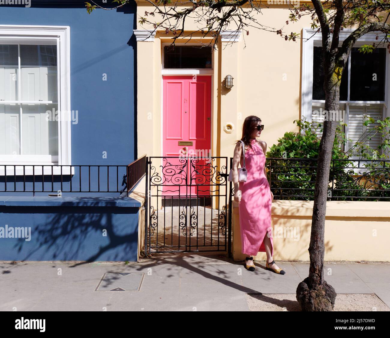Londra, Greater London, Inghilterra, aprile 09 2022: Donna in abito rosa si erge di fronte a una casa con una porta rosa su Portabello Road a Notting Hill. Foto Stock
