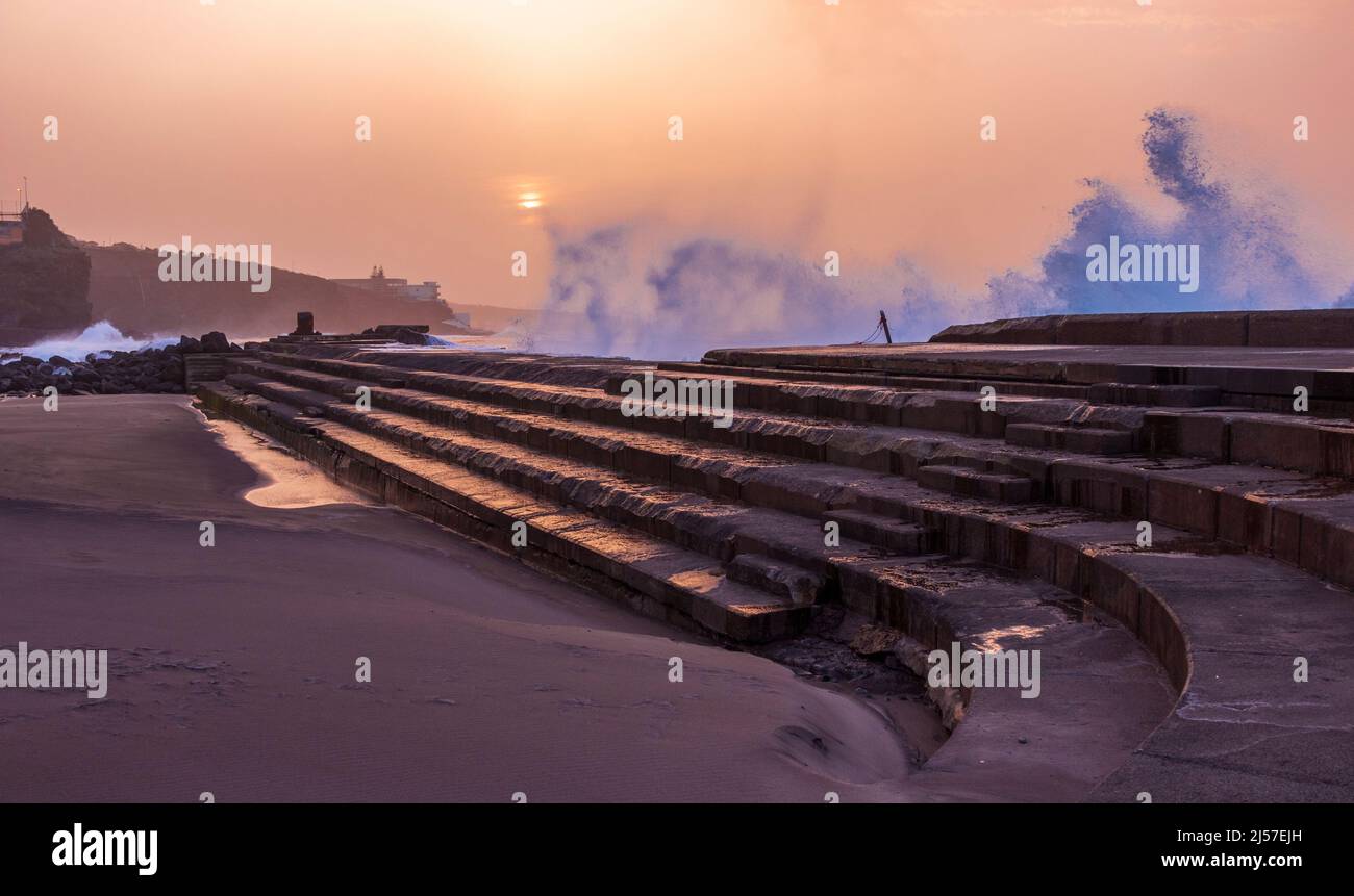 Onde che si infrangono sui gradini della piscina di mare naturale al tramonto a Bajamar, a nord delle Isole Canarie di Tenerife Foto Stock