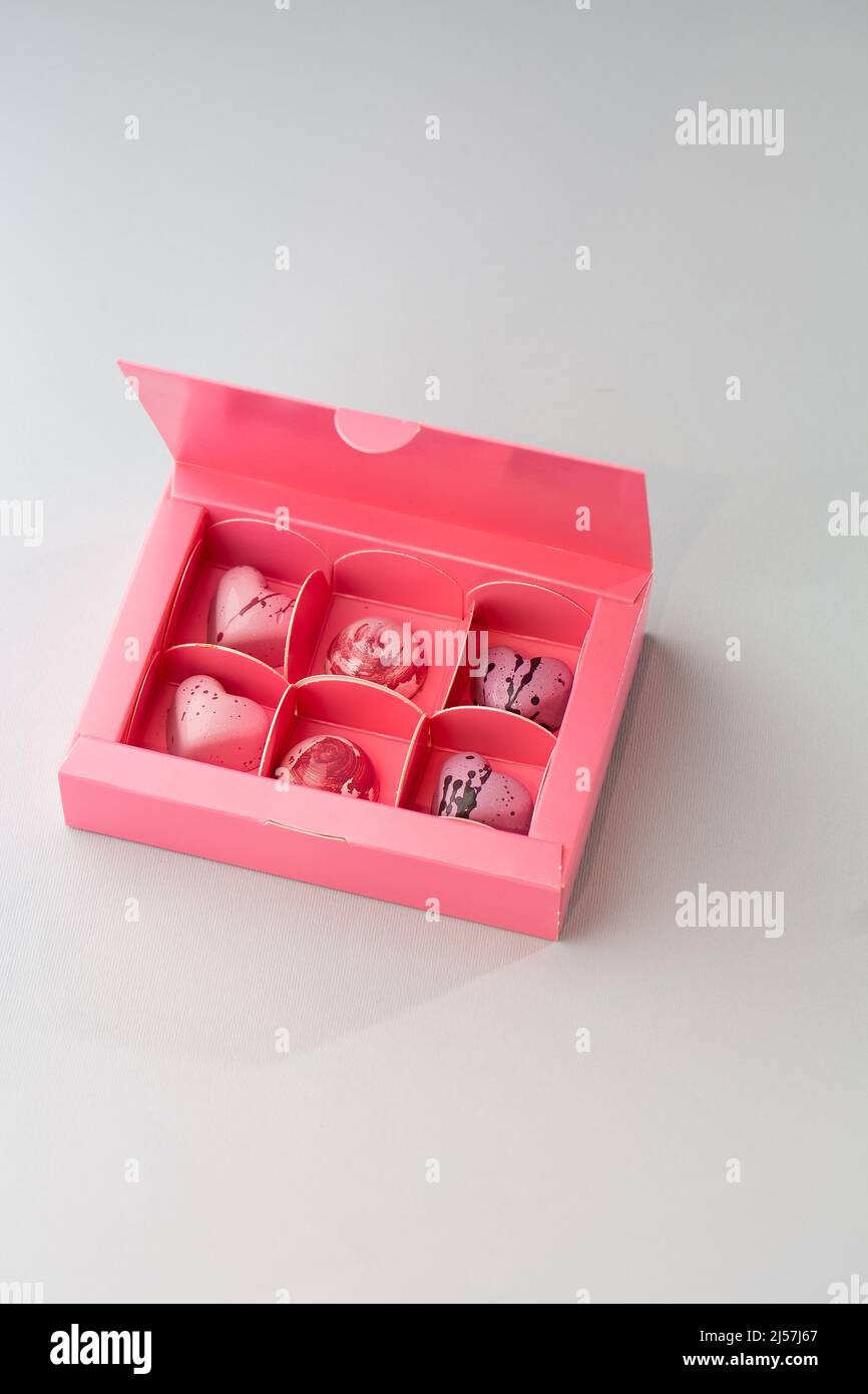 Caramelle al cioccolato fatte a mano di lusso in scatola rosa isolata su sfondo scuro. Esclusivo bonbon artigianale. Concetto di pubblicità di prodotto per pasticceria Foto Stock