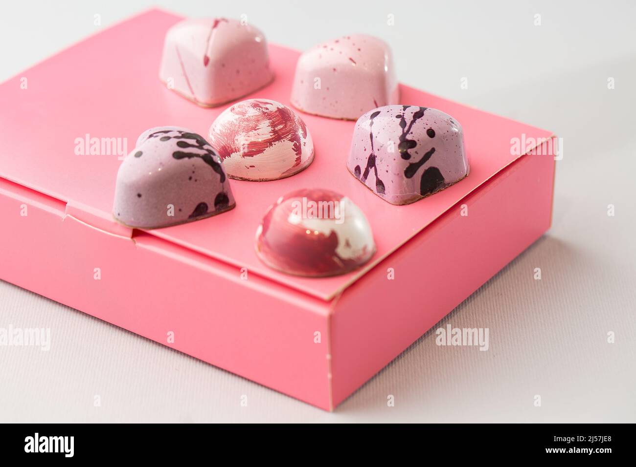 Caramelle di lusso al cioccolato fatte a mano su scatola rosa isolata su sfondo bianco. Esclusivo bonbon artigianale. Concetto di pubblicità di prodotto per pasticceria. Foto Stock