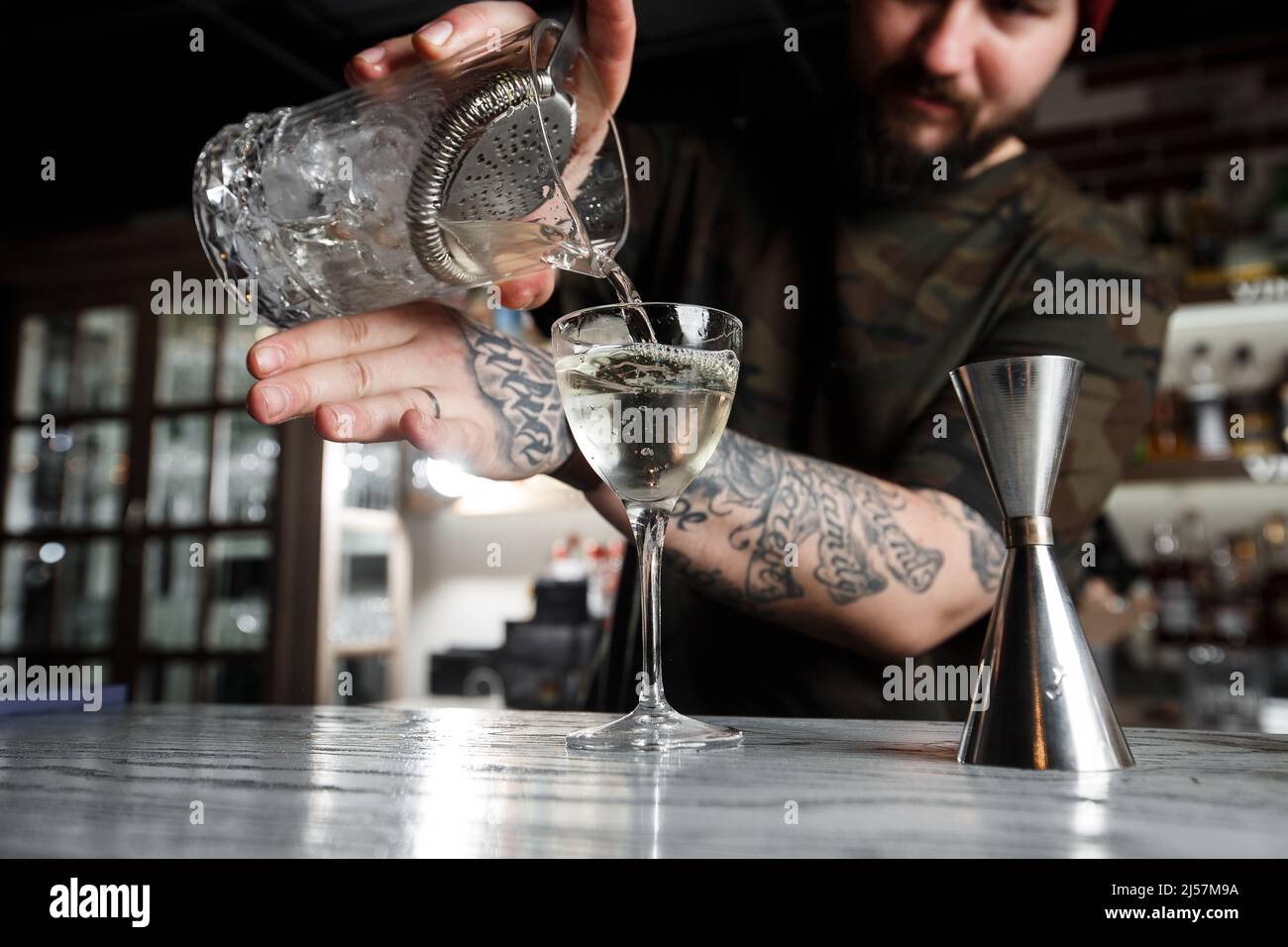 Barista versare un alcol dal bicchiere graduato attraverso il filtro a rete  al cocktail sul bancone bar sullo sfondo sfocato Foto stock - Alamy