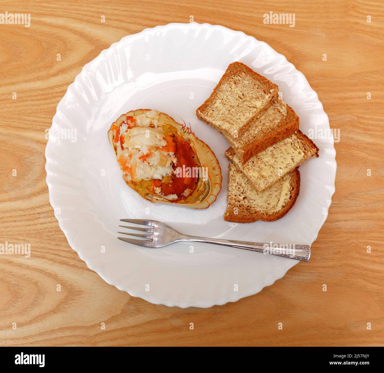 Un piatto con un granchio vestito accompagnato da fette di pane integrale marrone per un pranzo leggero. Foto Stock