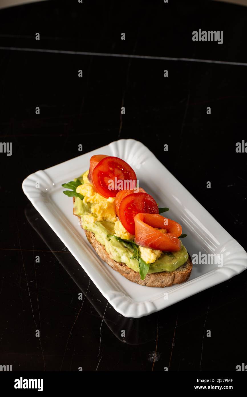 Pane tostato con un uovo, un avocado a fette, un salmone, pomodori e lattuga. Menu dietetico. Disposizione piatta. Foto Stock