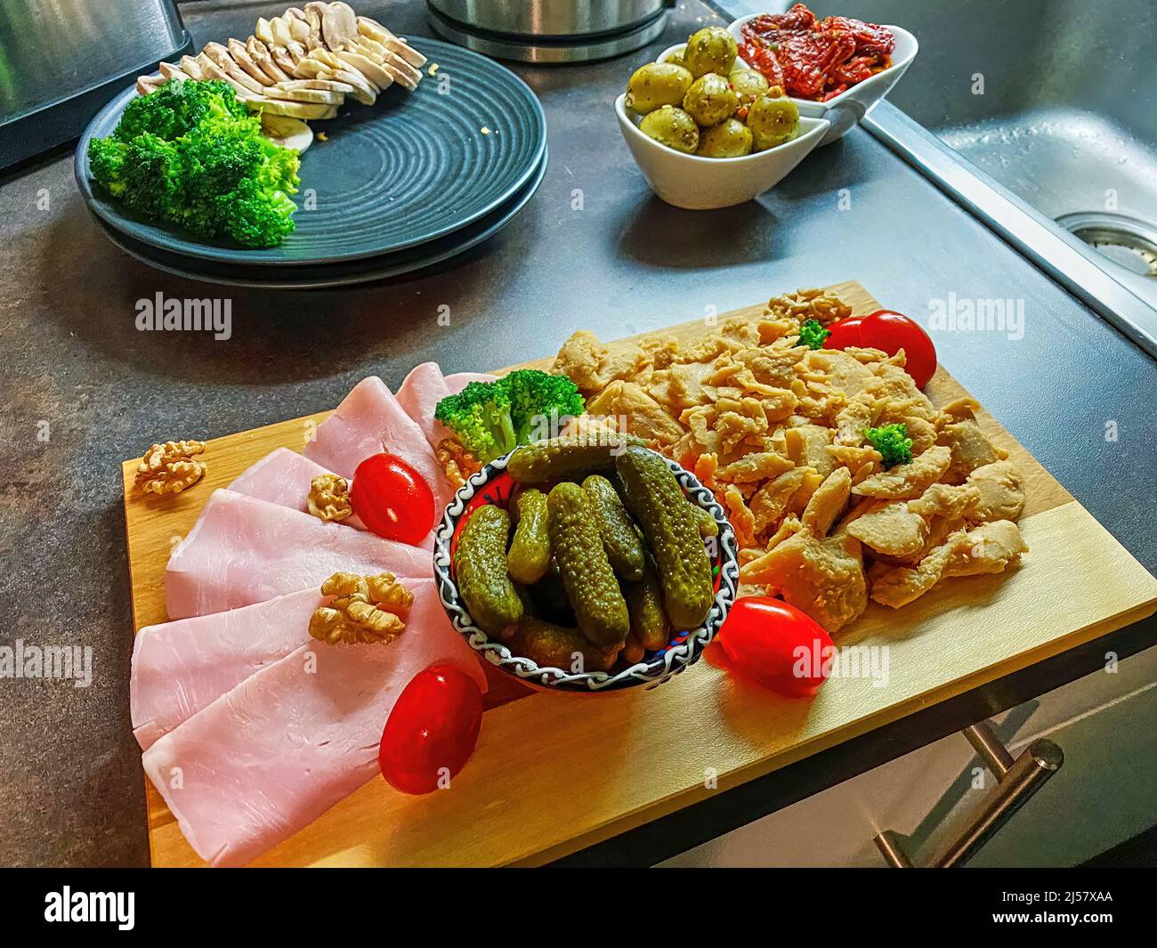 Tavola di legno su cui vari alimenti come prosciutto, verdure e pollame vegano sono decorativamente disposti. Foto Stock