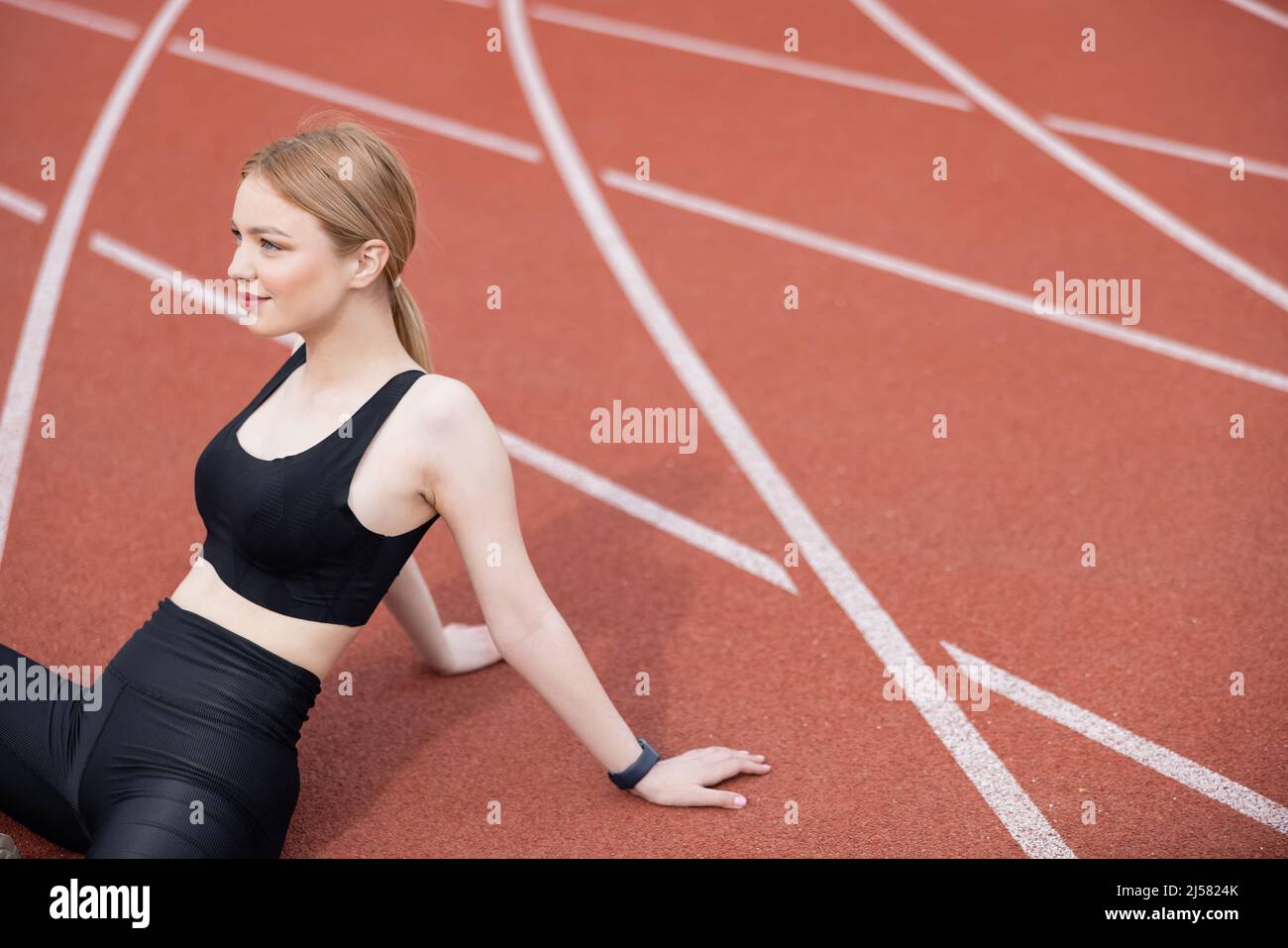 donna sportiva felice in reggiseno nero seduto sul campo sportivo Foto Stock