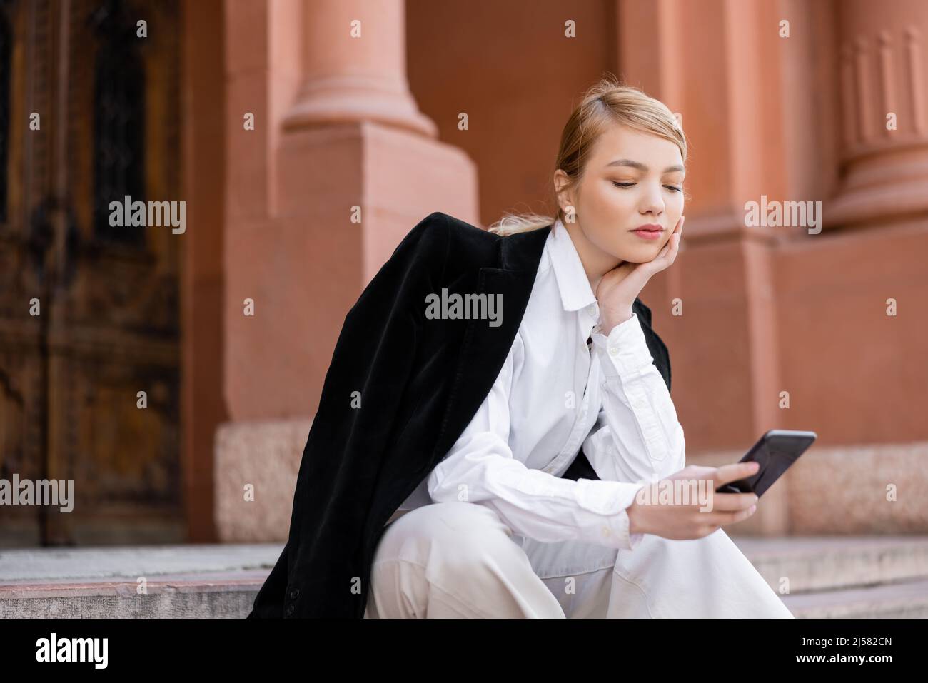 giovane donna in camicia bianca e blazer nero con smartphone su strada  urbana Foto stock - Alamy