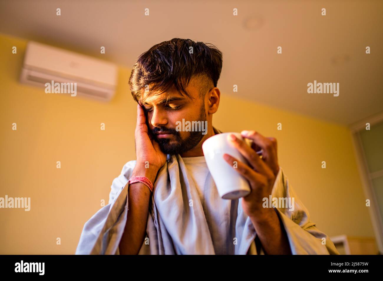 uomo indiano arabo che beve limone caldo dinder masala tè in camera da letto di mattina mentre la sensazione di freddo coperto con una coperta Foto Stock