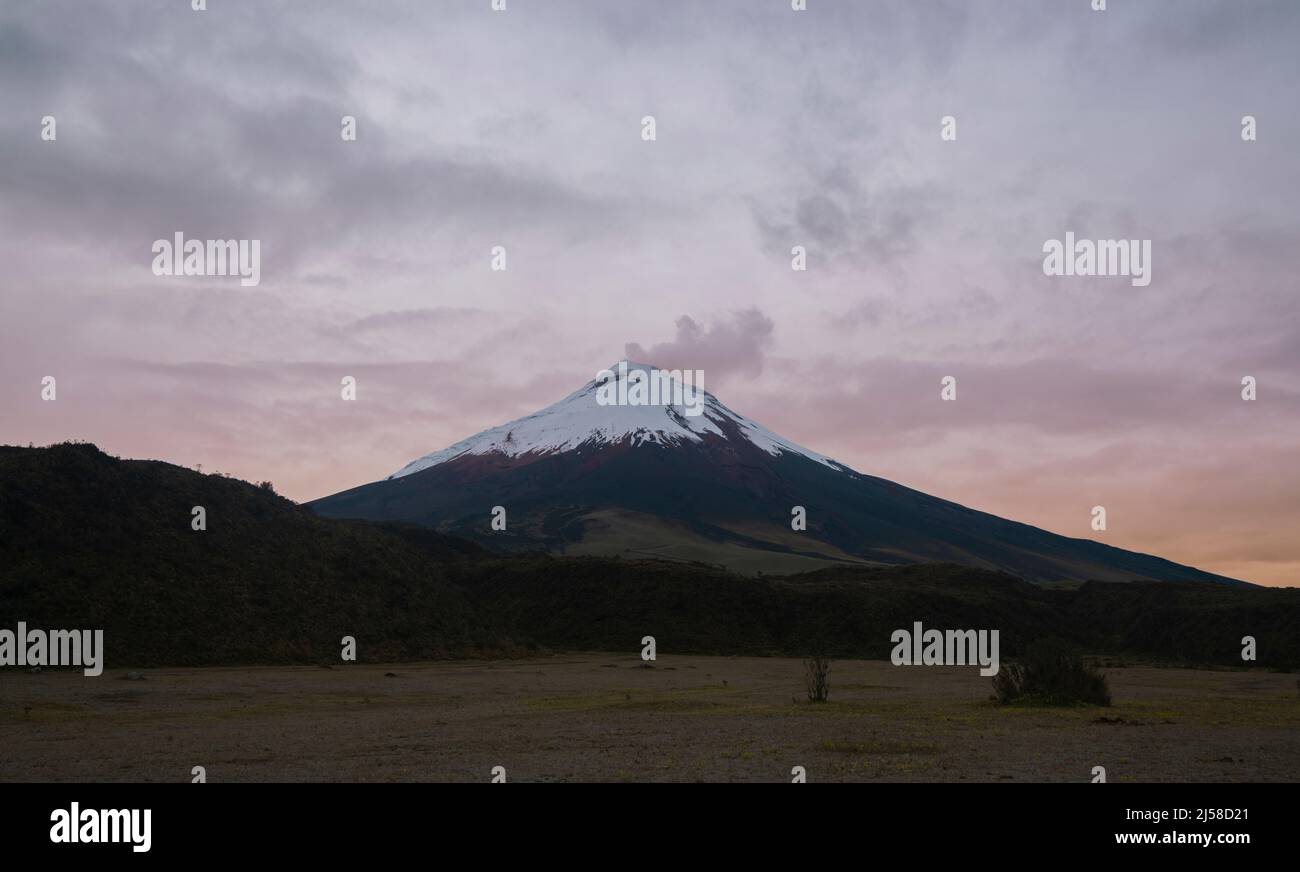Vista panoramica del vulcano Cotopaxi dietro un campo verde senza persone in un alba nuvoloso - Ecuador Foto Stock