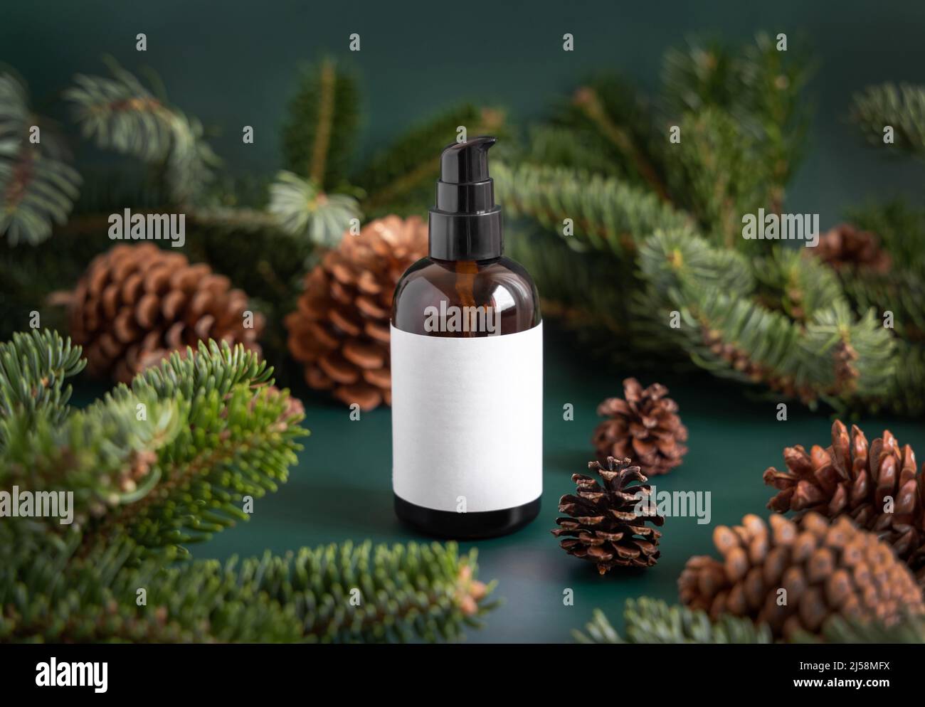 Vaso di vetro marrone vicino a rami di abete e coni di pino su verde scuro primo piano. Mockup di imballaggio del marchio. Un dispenser a pompa per prodotti per la cura della pelle, crema o ser Foto Stock
