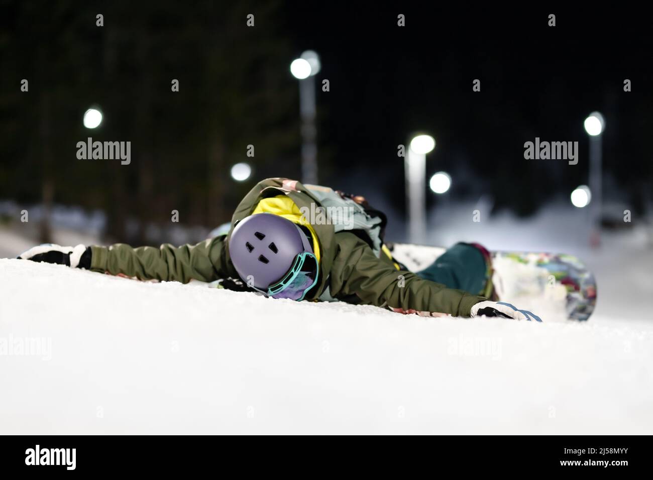 Ragazza snowboarder sdraiata a faccia in giù in pendenza. Sci notturno nella località invernale. Foto Stock