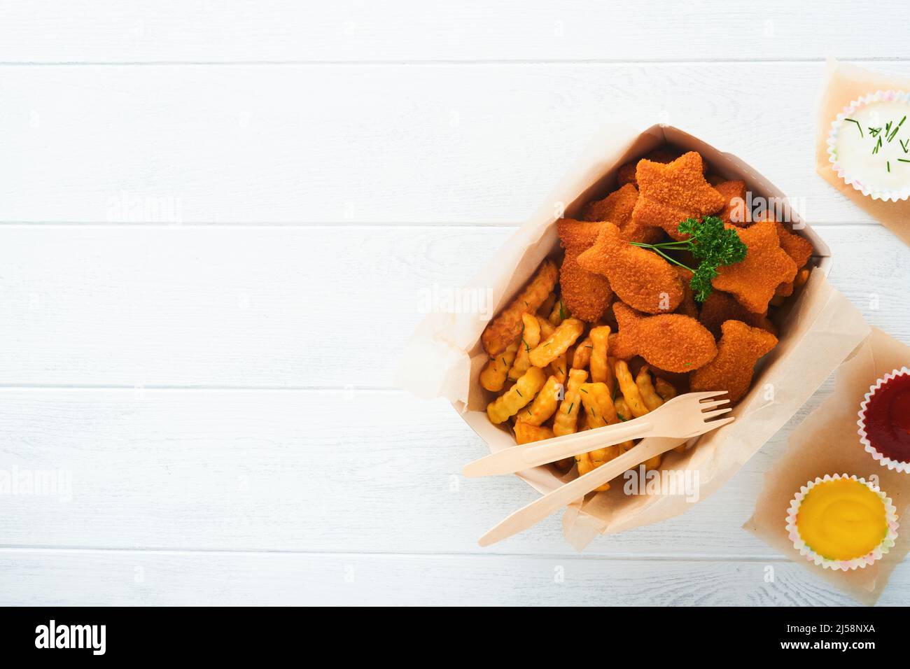 Fish and chips fast food britannico. Bastoncini di pesce con patatine fritte su piastra di carta da asporto su sfondo bianco in legno. Tradizionale britannico autentico Foto Stock