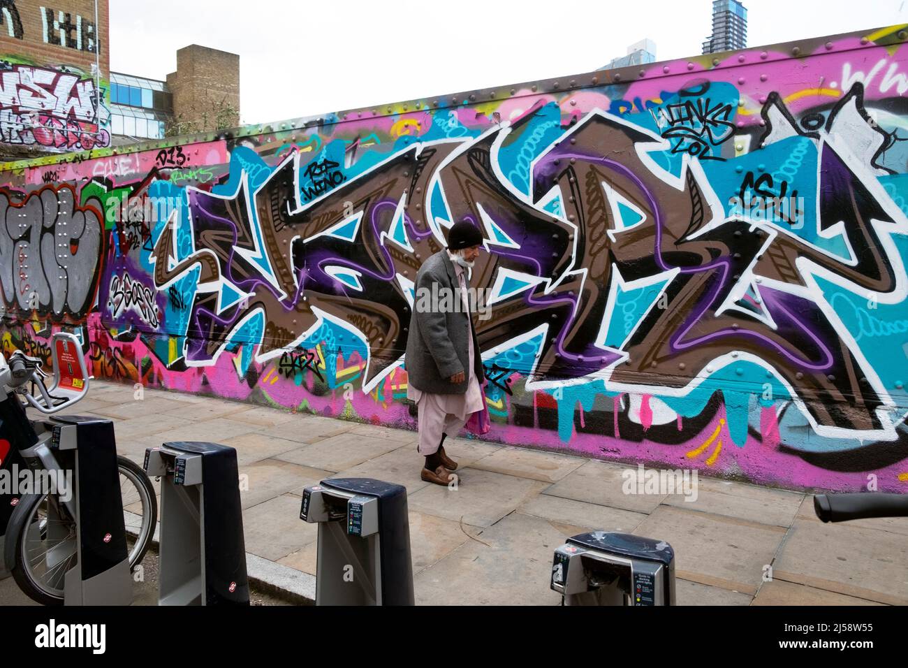 Persone persona a piedi da colorati graffiti pittura su hoardings in Brick Lane Shoreditch primavera Aprile 2022 Londra Inghilterra Regno Unito KATHY DEWITT Foto Stock