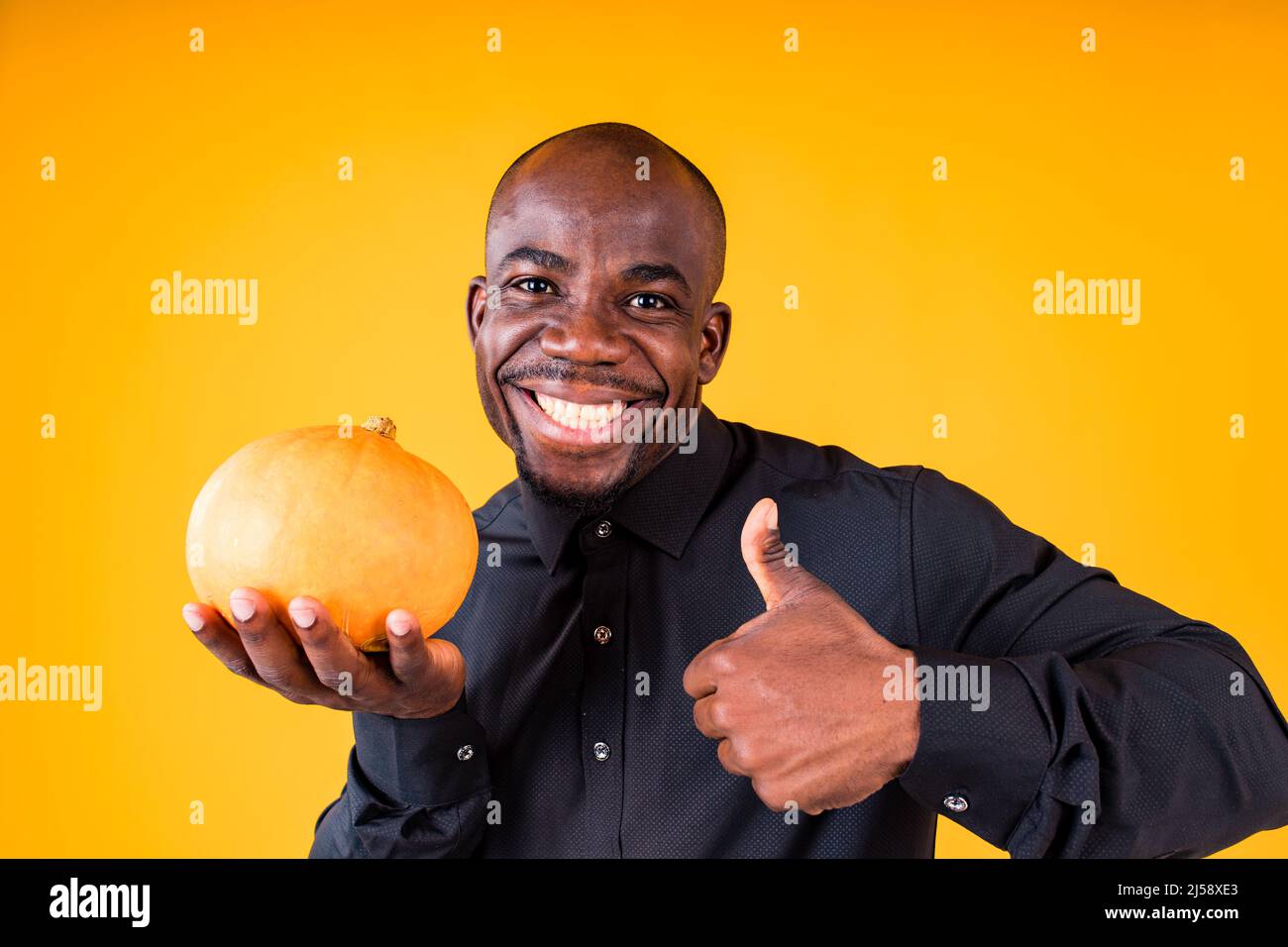 People e Halloween preparazione concetto, uomo che tiene piccola zucca in studio sfondo giallo Foto Stock