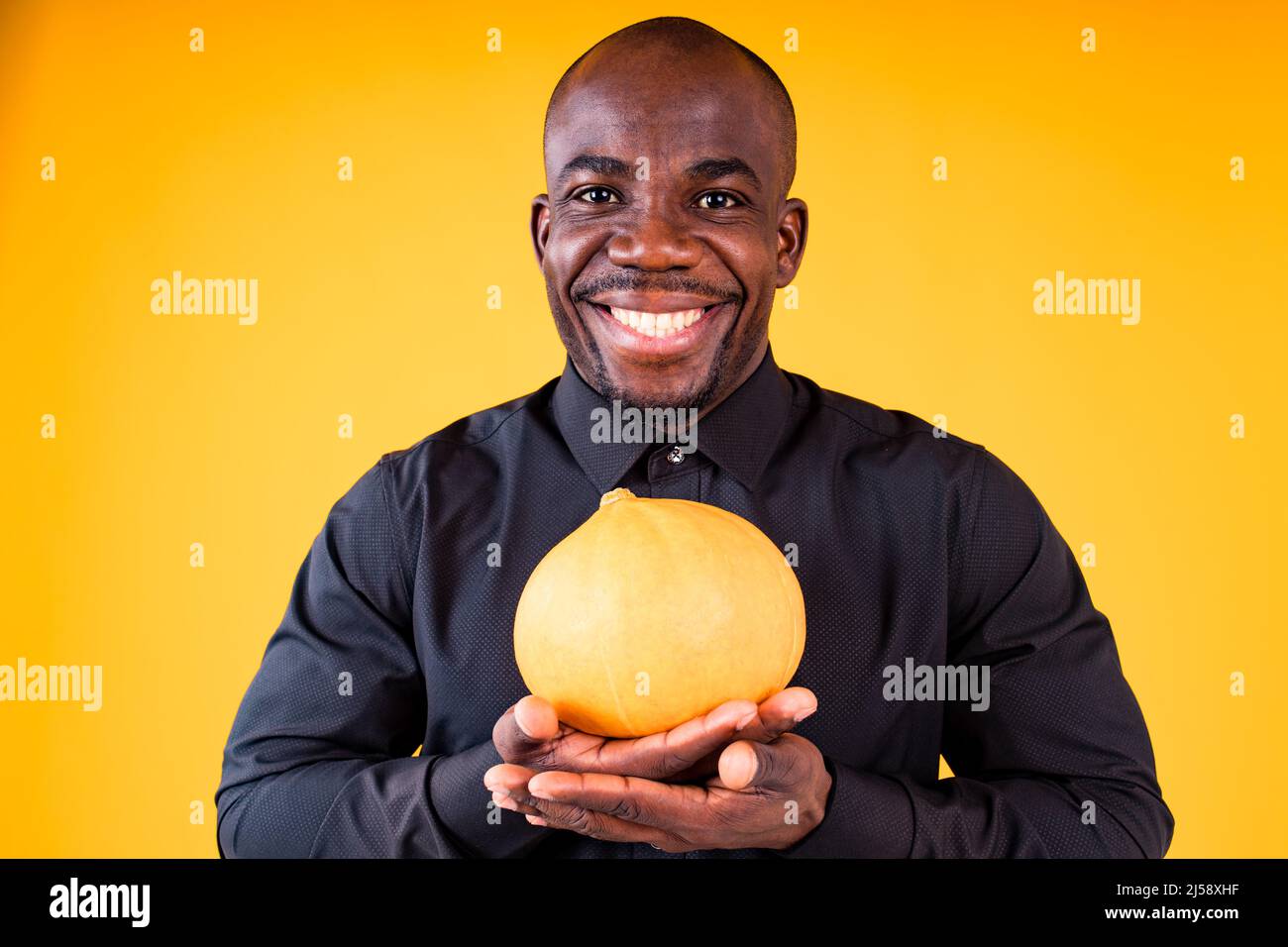 People e Halloween preparazione concetto, uomo che tiene piccola zucca in studio sfondo giallo Foto Stock