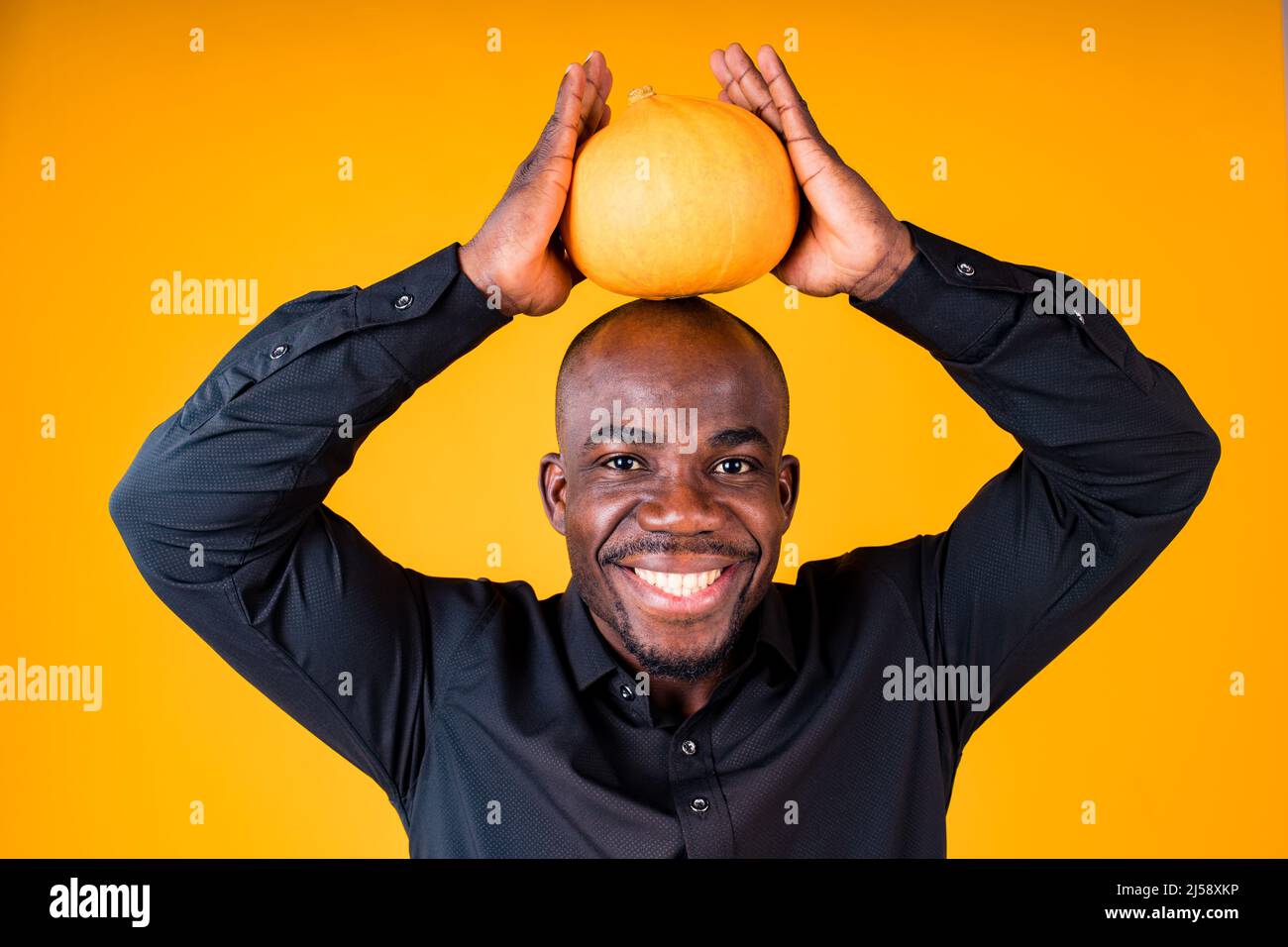 People e Halloween preparazione concetto, uomo che tiene piccola zucca in studio sfondo giallo Foto Stock