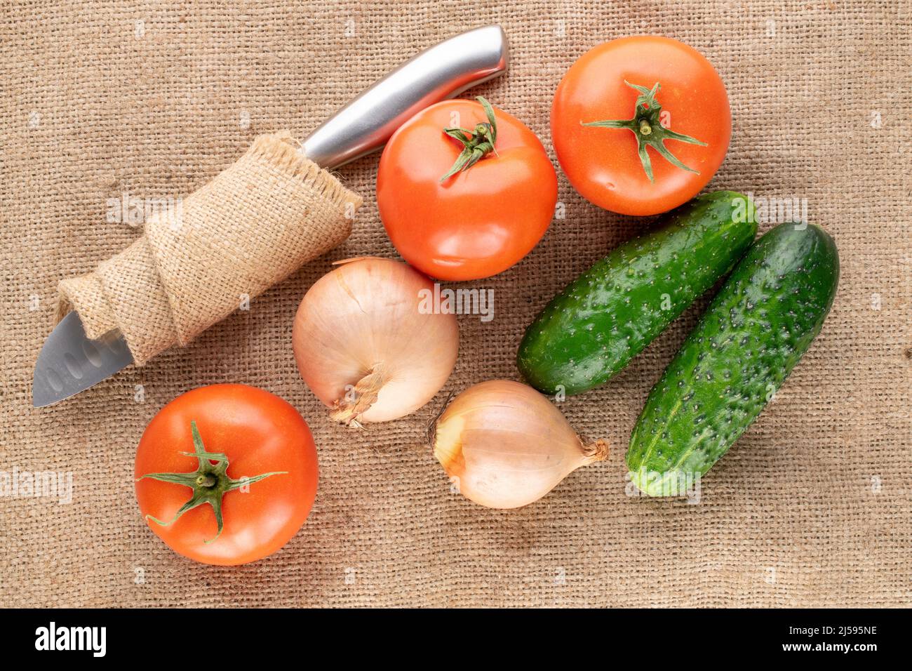 Tre pomodori maturi, due cipolle e due cetrioli in tessuto di iuta, macro, vista dall'alto. Foto Stock