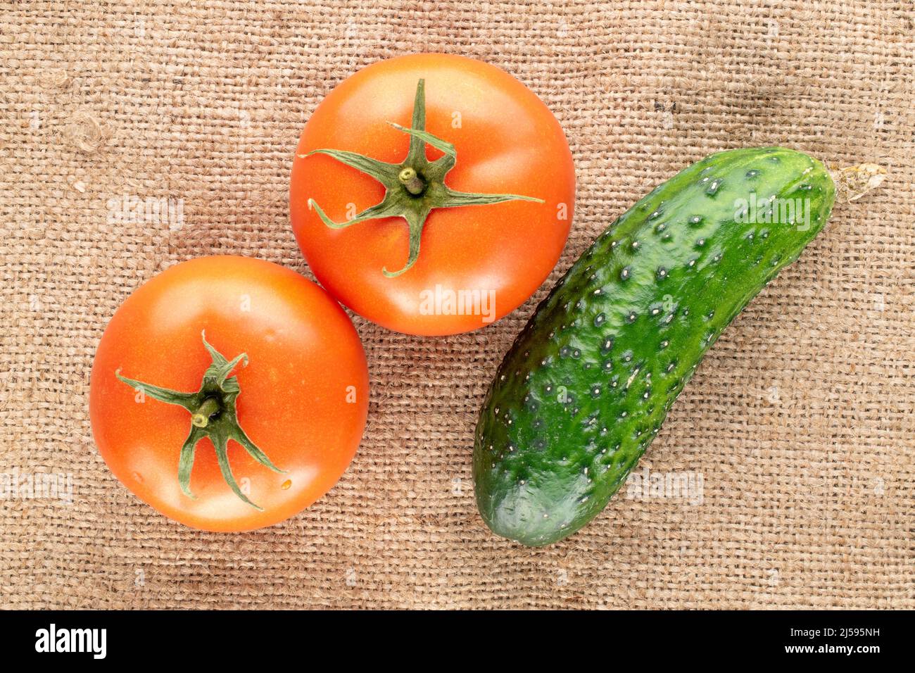 Due pomodori biologici e cetrioli su tessuto di iuta, macro, vista dall'alto. Foto Stock