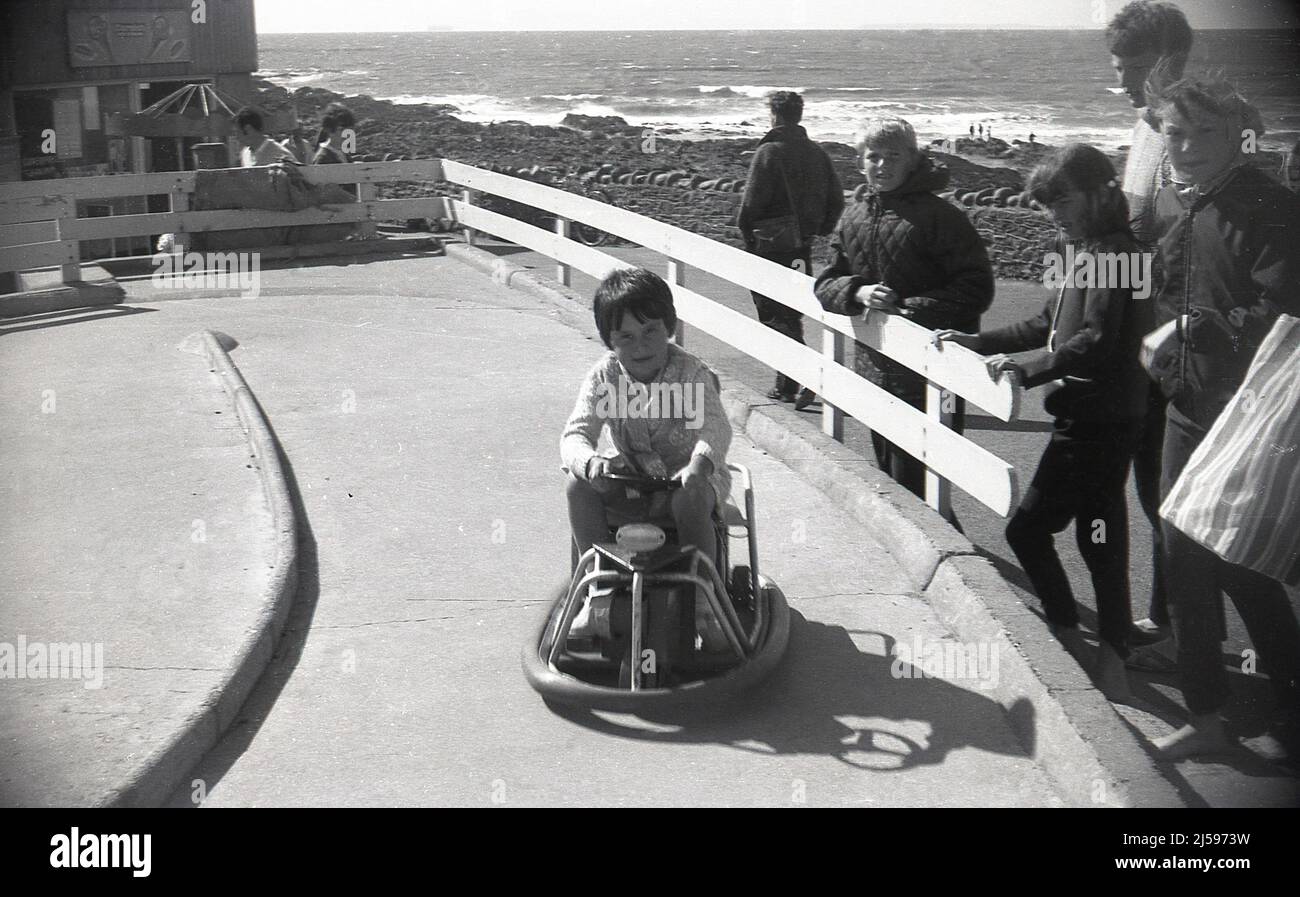 1960s, storica, al mare, una giovane ragazza che guida su un mini go-kart alimentato a batteria in una pista di cemento, Inghilterra, Regno Unito. Foto Stock