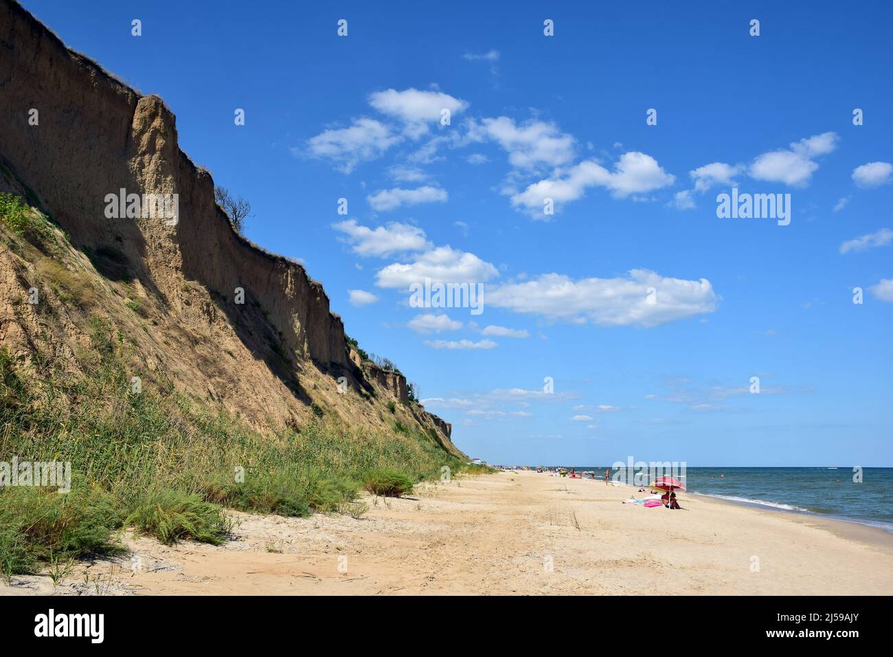 Le onde di mare schiumose rotolano sulla spiaggia di sabbia diurna. I turisti si prendono il sole e nuotano in lontananza Foto Stock