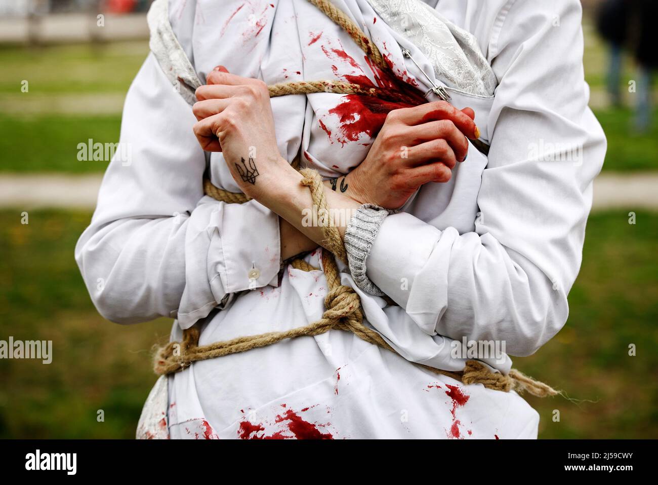 Berlino, Germania. 21st Apr 2022. Un partecipante ha un tatuaggio dello stemma ucraino in mano, come dimostra con le mani legate insieme ad altre donne in abiti bianchi con sangue falso su di loro e ha Unito le mani a una dimostrazione contro la violenza contro le donne e le ragazze in russo Guerra di aggressione contro l'Ucraina. Credit: Carsten Koall/dpa/Alamy Live News Foto Stock