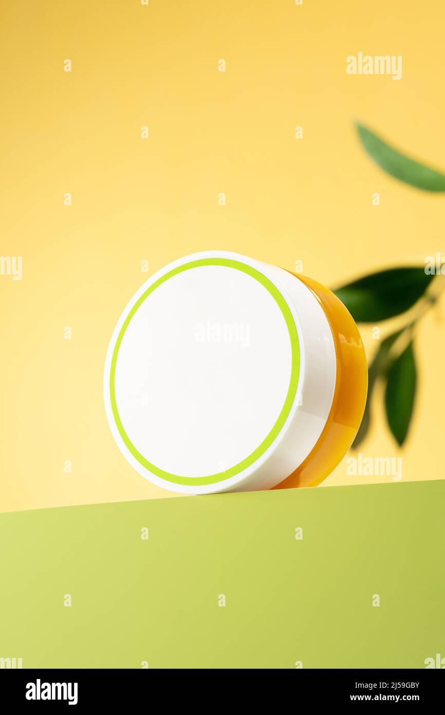 Una lattina di balsamo di piede con grasso di lana di pecora. Lanolina cosmetici per l'auto-cura, un vaso di cera impermeabilizzante su un podio verde chiaro. Sfondo giallo. Foto Stock