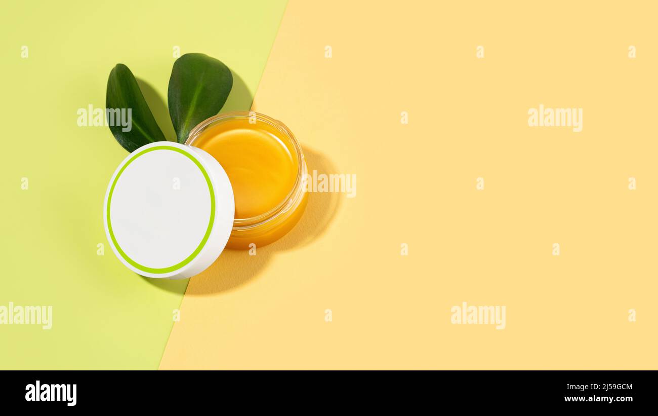 Un barattolo aperto di balsamo di piede con grasso di lana di pecora. Lanolina cosmetici per auto-cura, un vaso di cera impermeabilizzante su sfondo verde chiaro e beige. Foto Stock