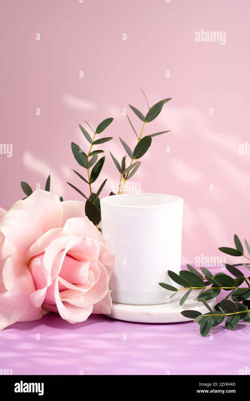 Composizione di fiori e candela fatta a mano in cera di soia ecologica e vegana su sfondo rosa. Candela di soia con rosa e foglie di viola chiaro Foto Stock