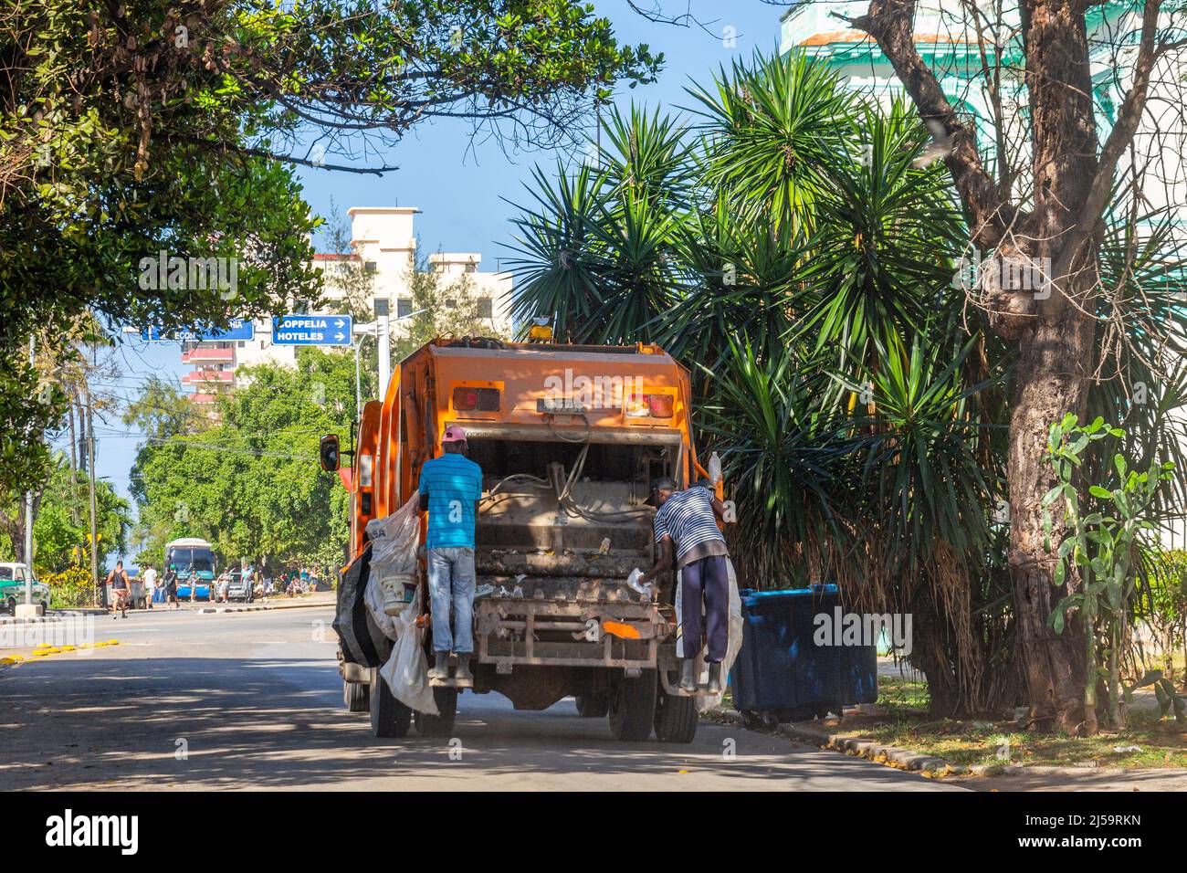 Due uomini cubani sono visti lavorare in un camion urbano della spazzatura nella capitale. Sullo sfondo si vede un viale centrale Foto Stock