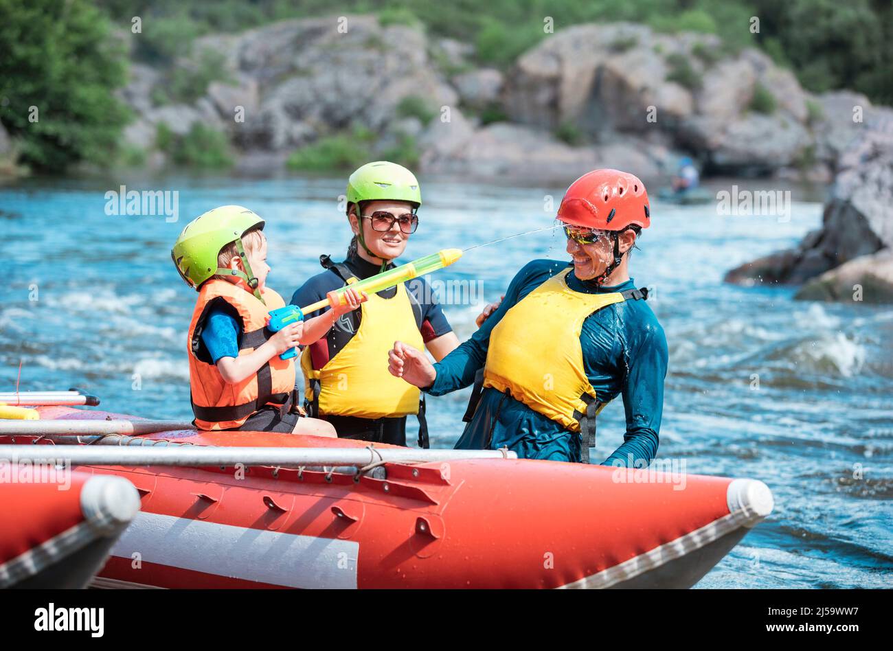 Madre, padre e figlio piccolo che gioca con pistole d'acqua a canottaggio gonfiabile catamarano Foto Stock