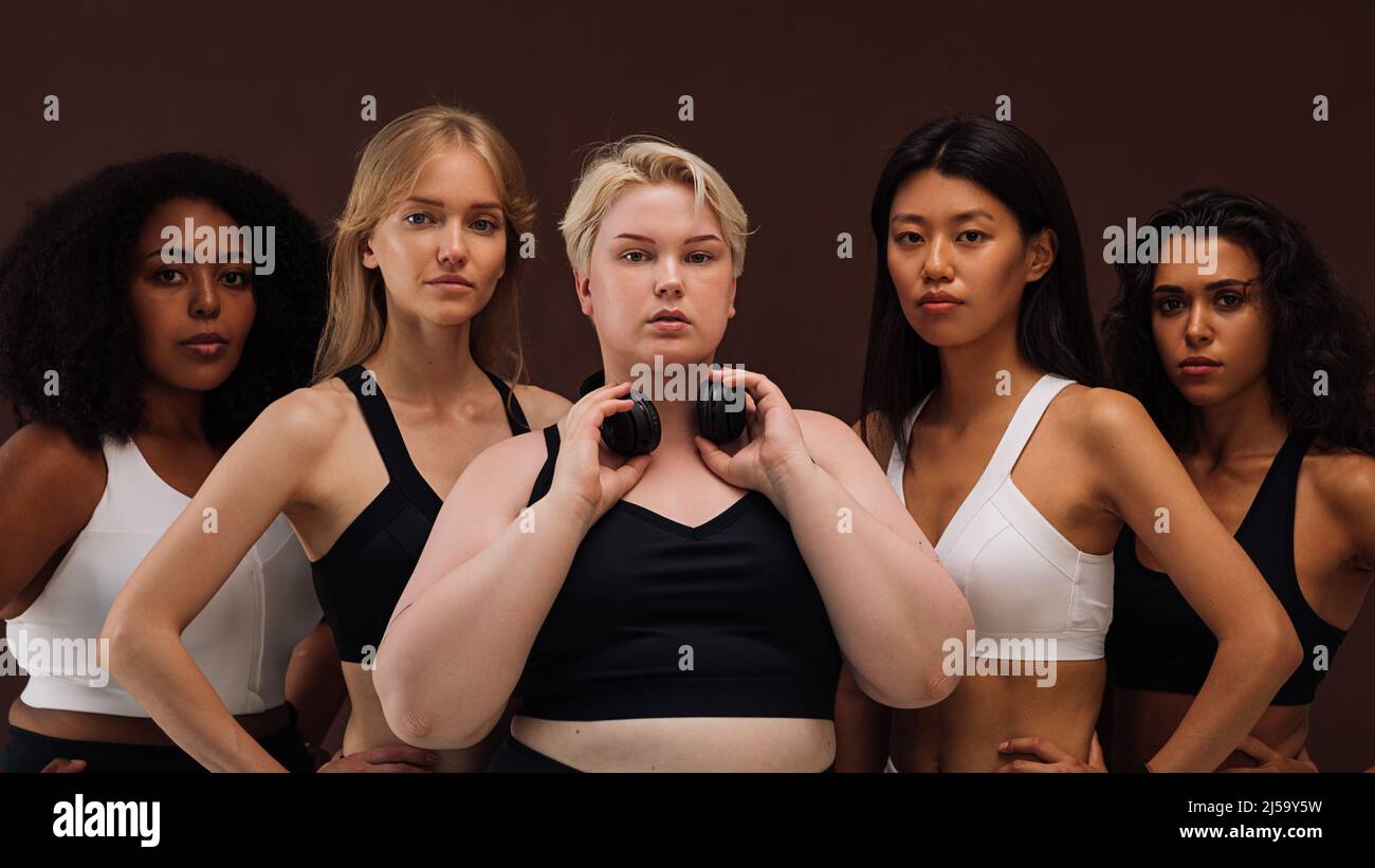 Ritratto di gruppo di giovani donne sicure in abiti sportivi in piedi insieme su sfondo marrone Foto Stock