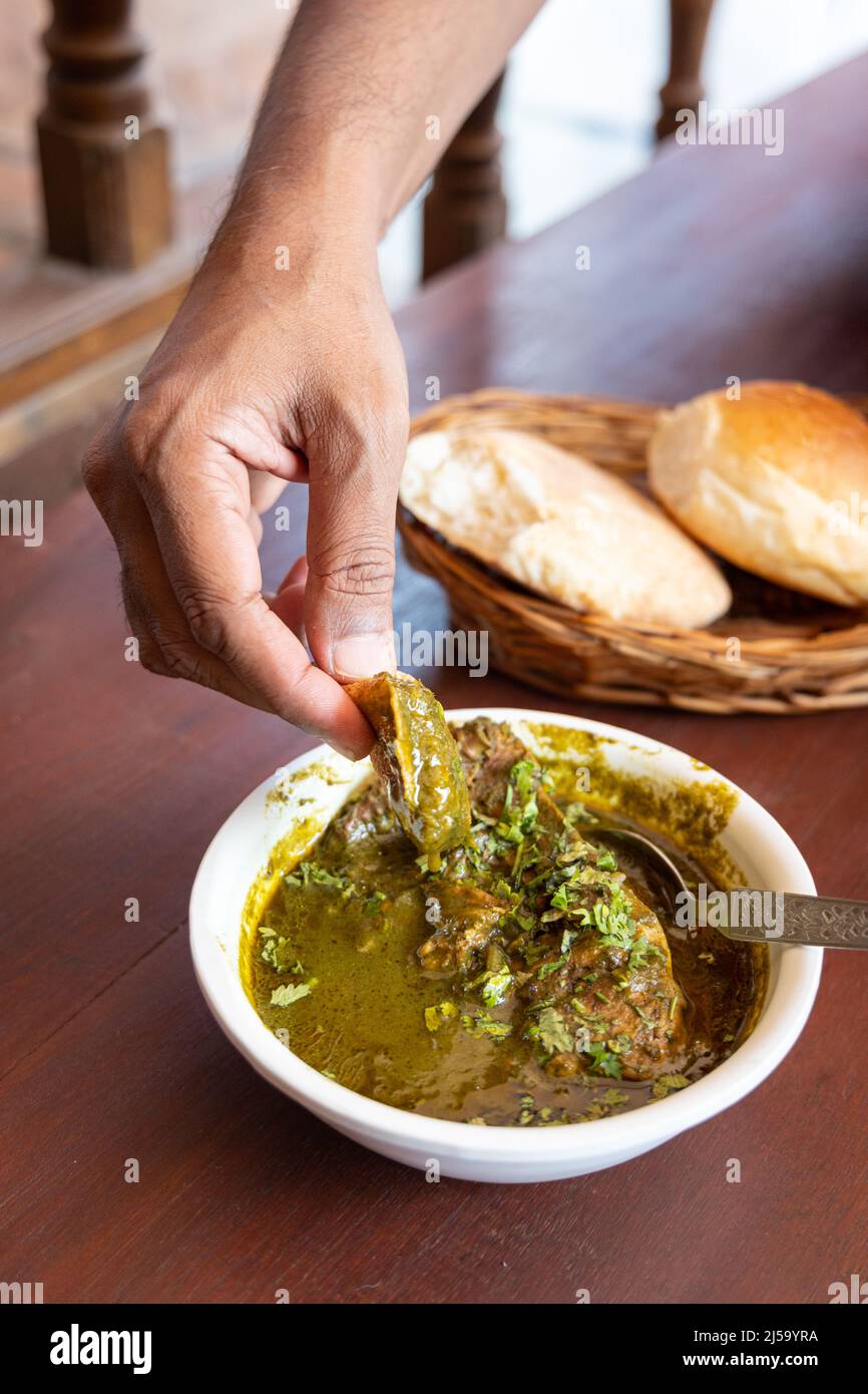 Mano umana che immerga un pezzo di pane di Goa in autentico piatto di Goa chiamato Chicken Cafreal. Foto Stock