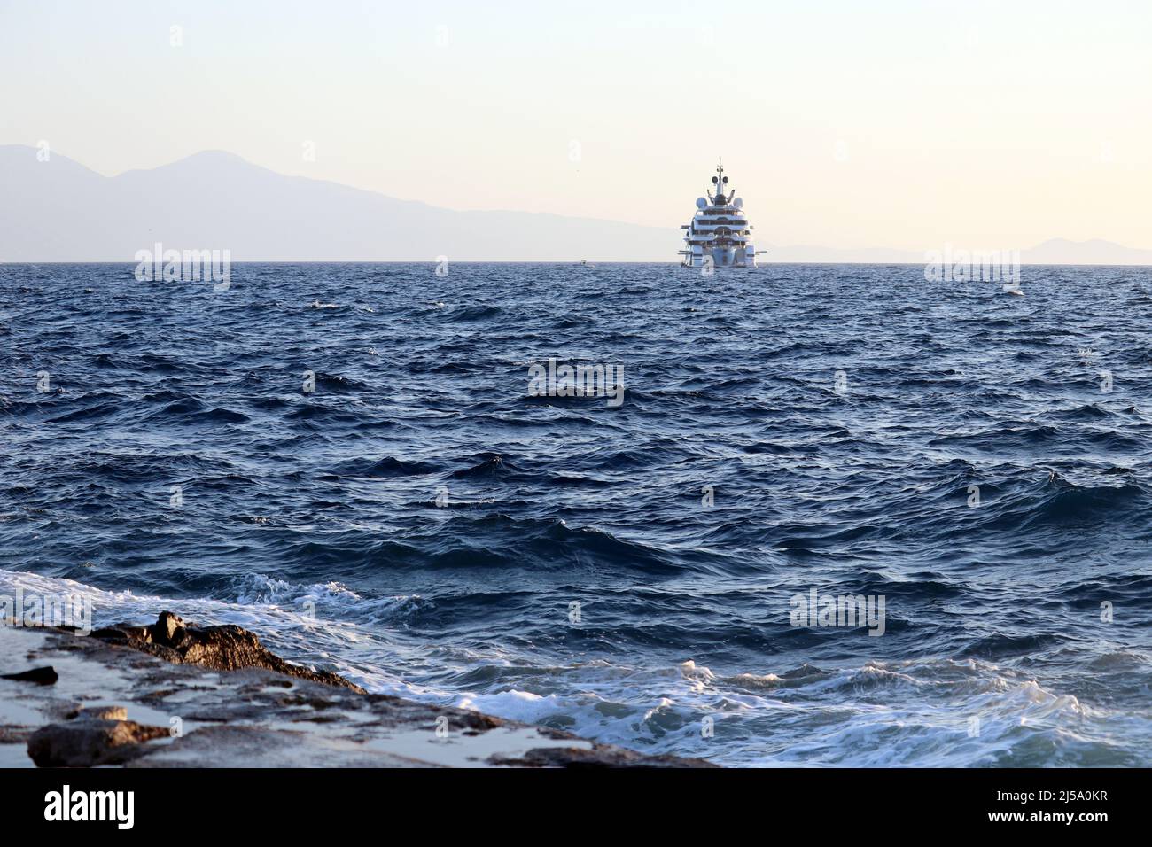 Vista dalla spiaggia di pietra alle onde del mare e silhouette dello yacht a vela. Barca di lusso su sfondo di montagne nebbie al mattino Foto Stock