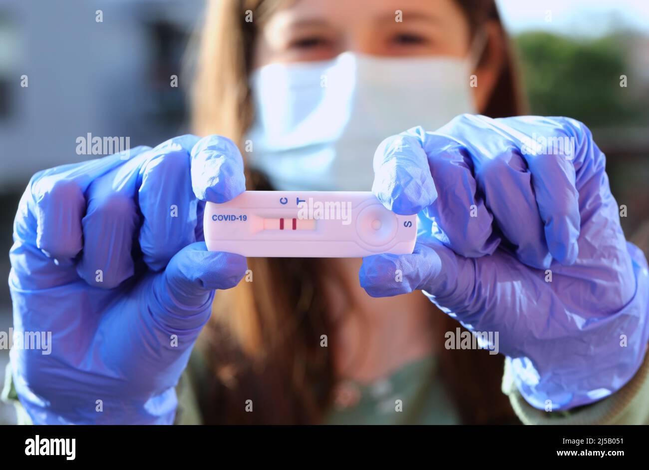 giovane donna con maschera chirurgica mantiene il test diagnostico del coronavirus tra i guanti in lattice dopo il test riuscito Foto Stock