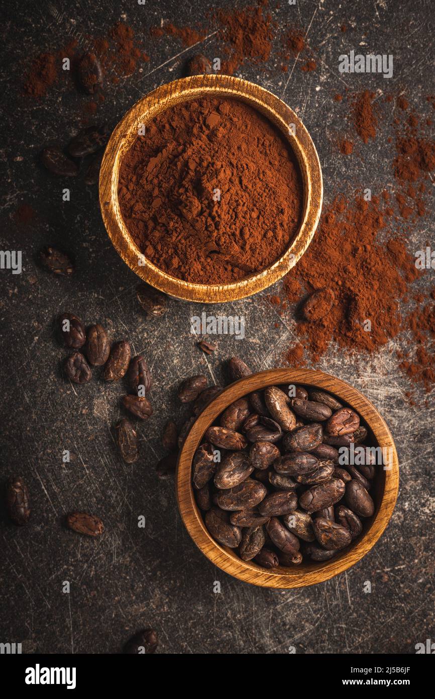 Cacao in grani e cacao in polvere in ciotole di legno su un tavolo nero. Vista dall'alto. Foto Stock
