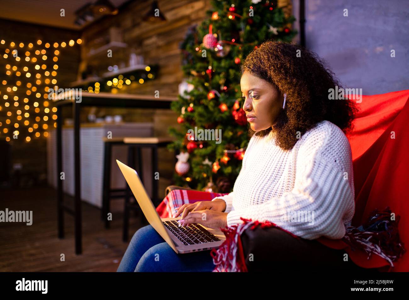 afro donna shopping online su laptop in accogliente interior.Preparing natale, bying sulle vendite invernali Foto Stock