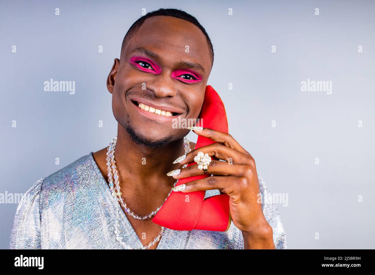 african american cross dressing trans drag queen con una scarpa rossa in studio parete bianca Foto Stock