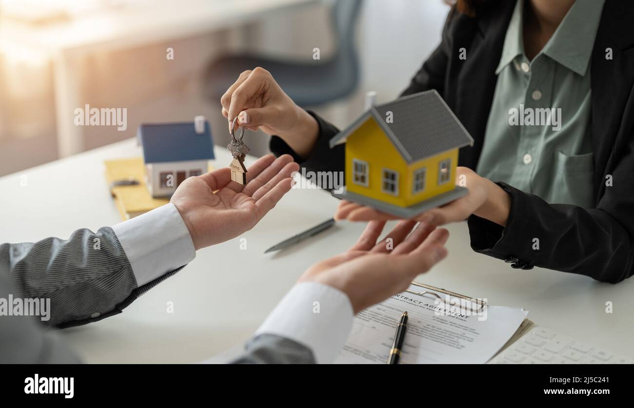 Uomo che prende le chiavi da agente di bene immobile femminile durante la riunione dopo la firma del contratto di affitto di affitto o del contratto di acquisto di vendita. Donna indipendente Foto Stock