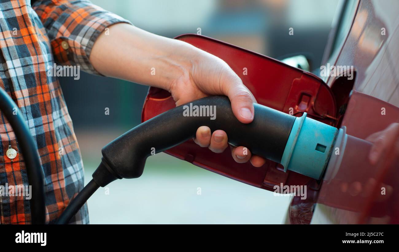 Il modello femmina si trova accanto a un'auto elettrica e contiene una spina di ricarica Foto Stock