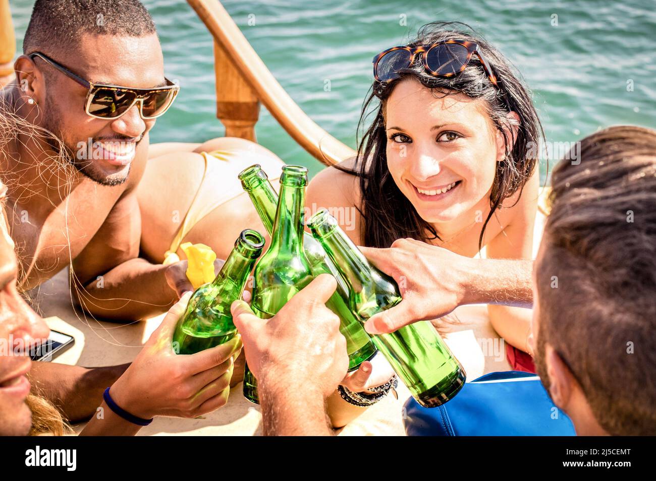 Multirazziale persone in yacht bere insieme - Gruppo di ricchi amici tostare birra e fare festa in barca a vela - concetto di viaggio di lusso con happ Foto Stock