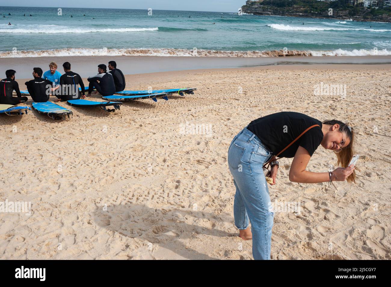 27 settembre 2019, Sydney, nuovo Galles del Sud, Australia - Una giovane donna si attende per scattare una foto su Bondi Beach mentre i surfboard prendono parte a una lezione di surf sullo sfondo. [traduzione automatizzata] Foto Stock