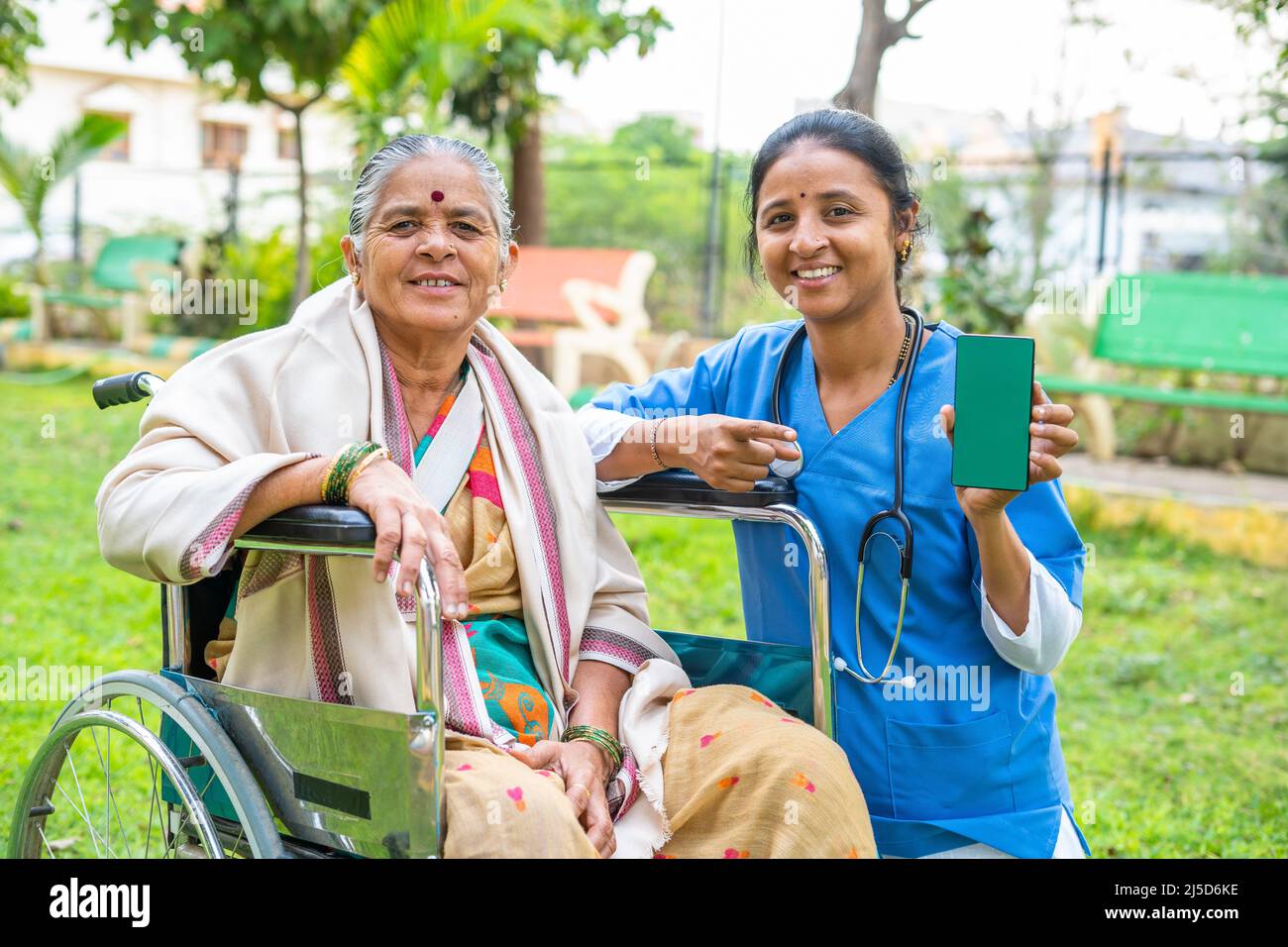 il medico mostra il telefono cellulare con schermo verde con il paziente seduto su sedia a rotelle al parco - concetto di tecnologia, promozione app per l'assistenza sanitaria e. Foto Stock