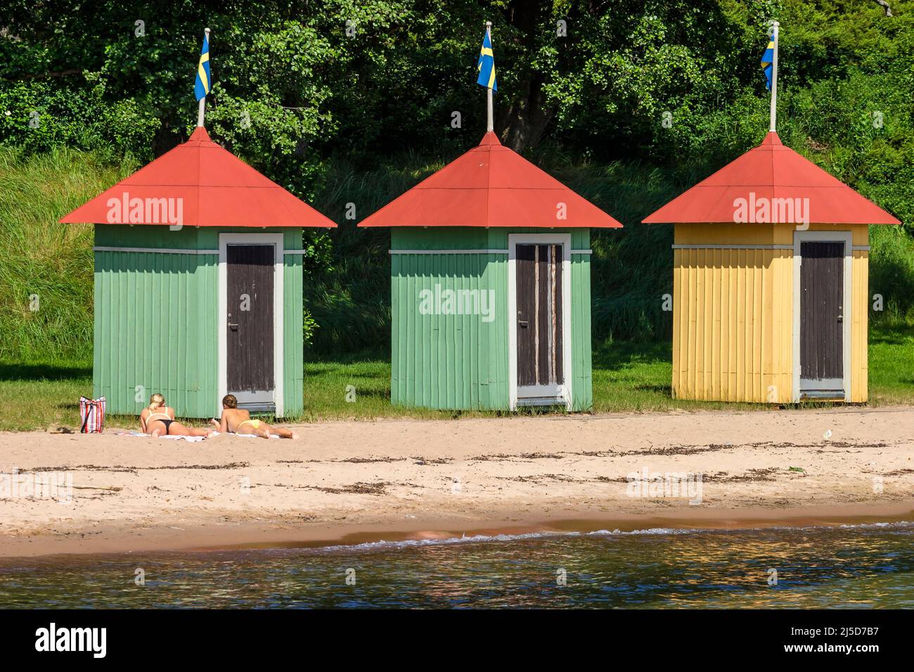 Giovani donne che prendono il sole presso una spiaggia di sabbia con cabine balneari Foto Stock