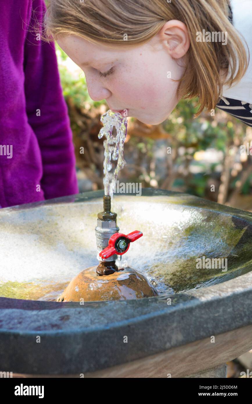 Giovane ragazza che beve un drink d'acqua / beve da una fontana di acqua pubblica dissetante all'esterno, in un parco cittadino, a Catania, in Sicilia. Italia. (129) Foto Stock