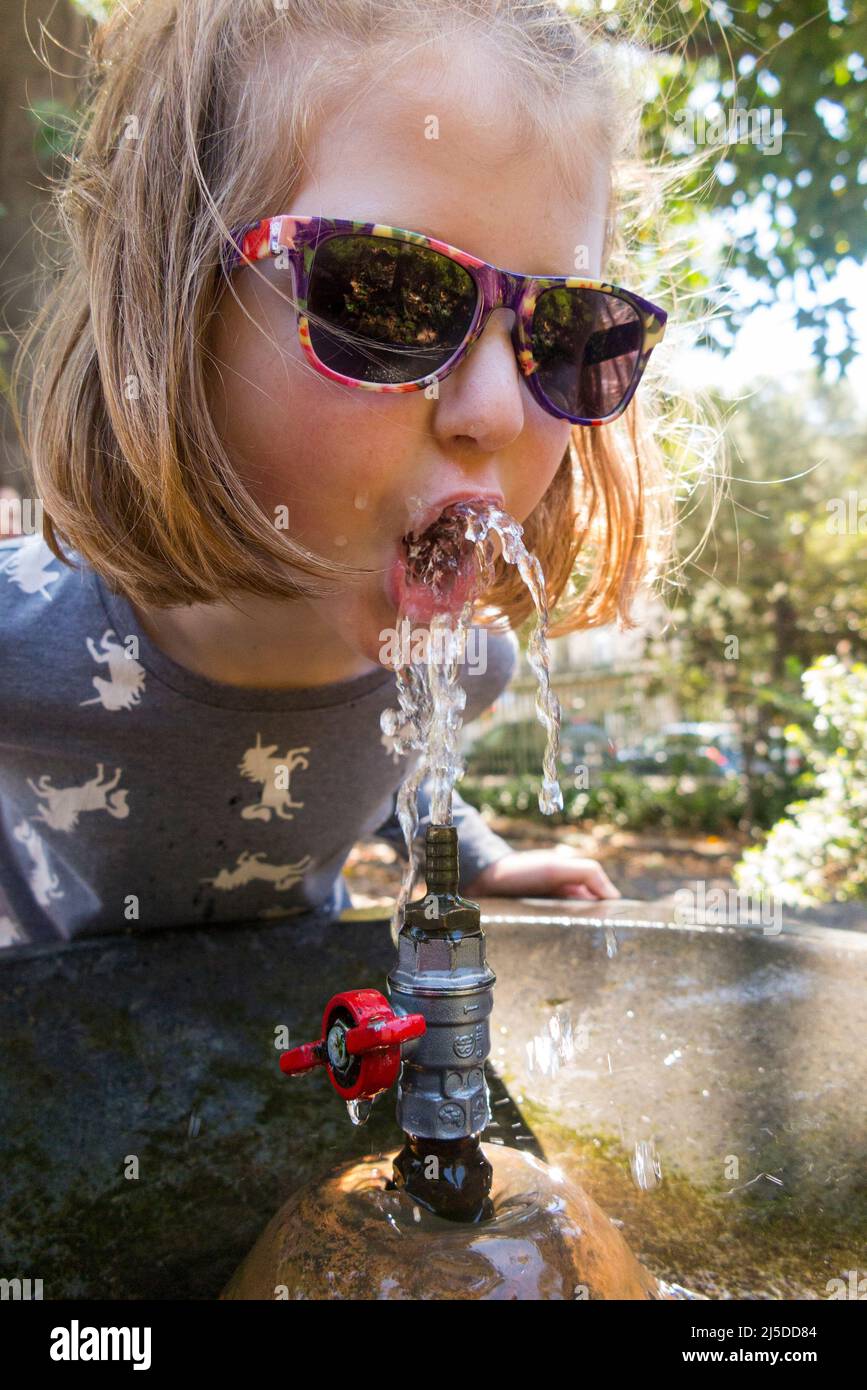 Giovane ragazza che beve un drink d'acqua / beve da una fontana di acqua pubblica dissetante all'esterno, in un parco cittadino, a Catania, in Sicilia. Italia. (129) Foto Stock