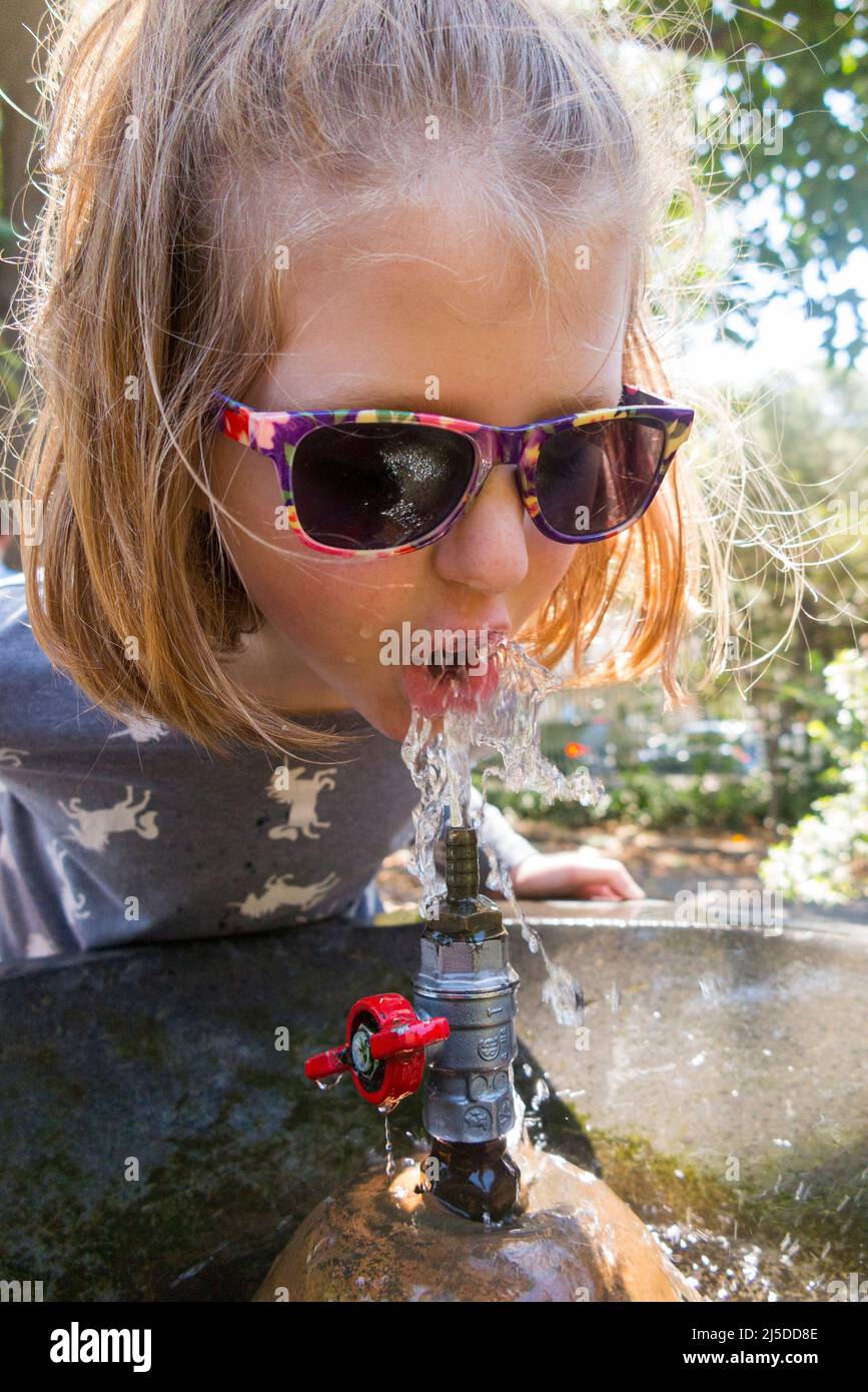 Giovane ragazza che beve un drink d'acqua / beve da una fontana di acqua pubblica dissetante all'esterno, in un parco cittadino, a Catania, in Sicilia. Italia. (129) Foto Stock